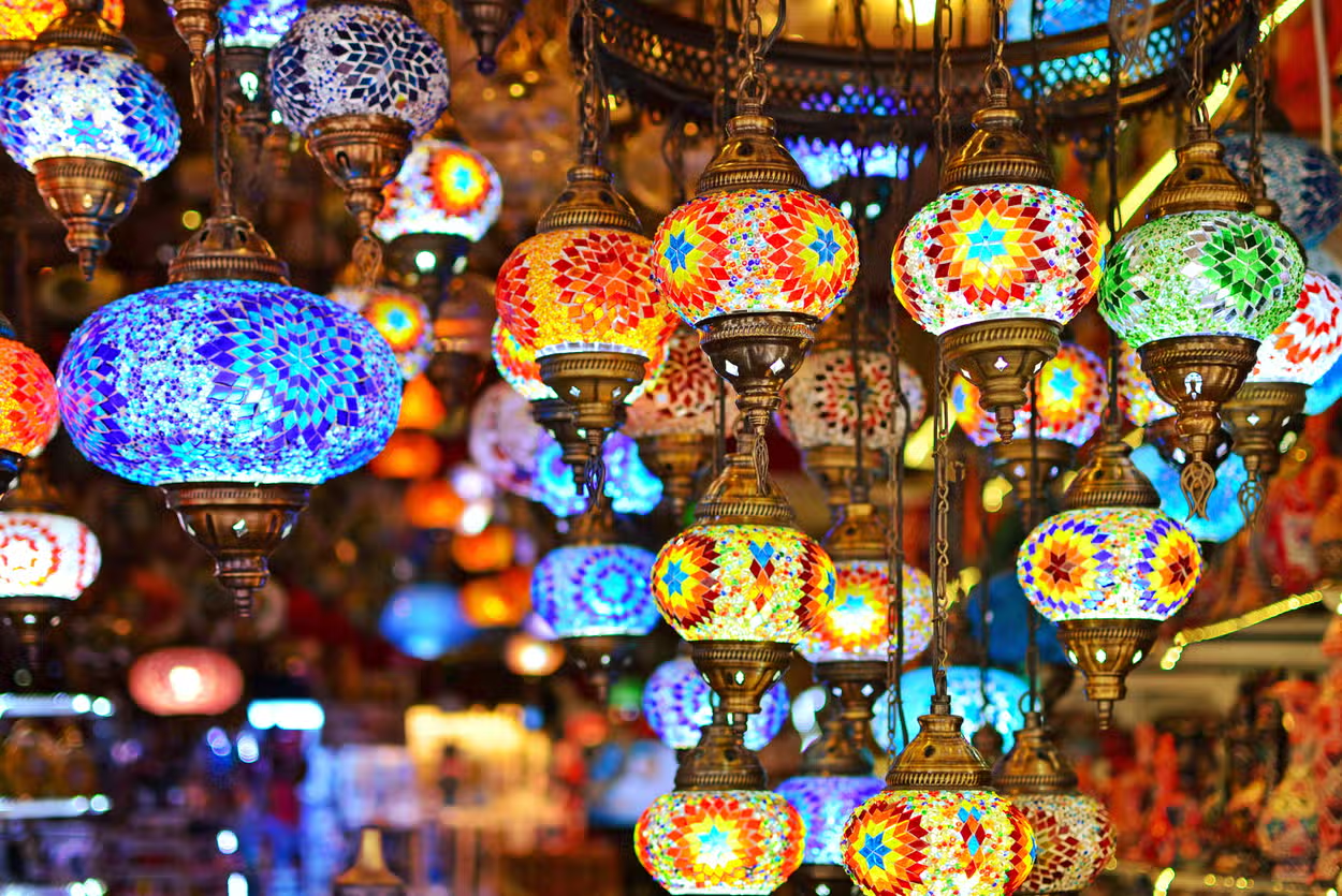 Cluster of lit Turkish mosaic lamps in red, blue, and amber glass hanging in a Grand Bazaar lamp alley